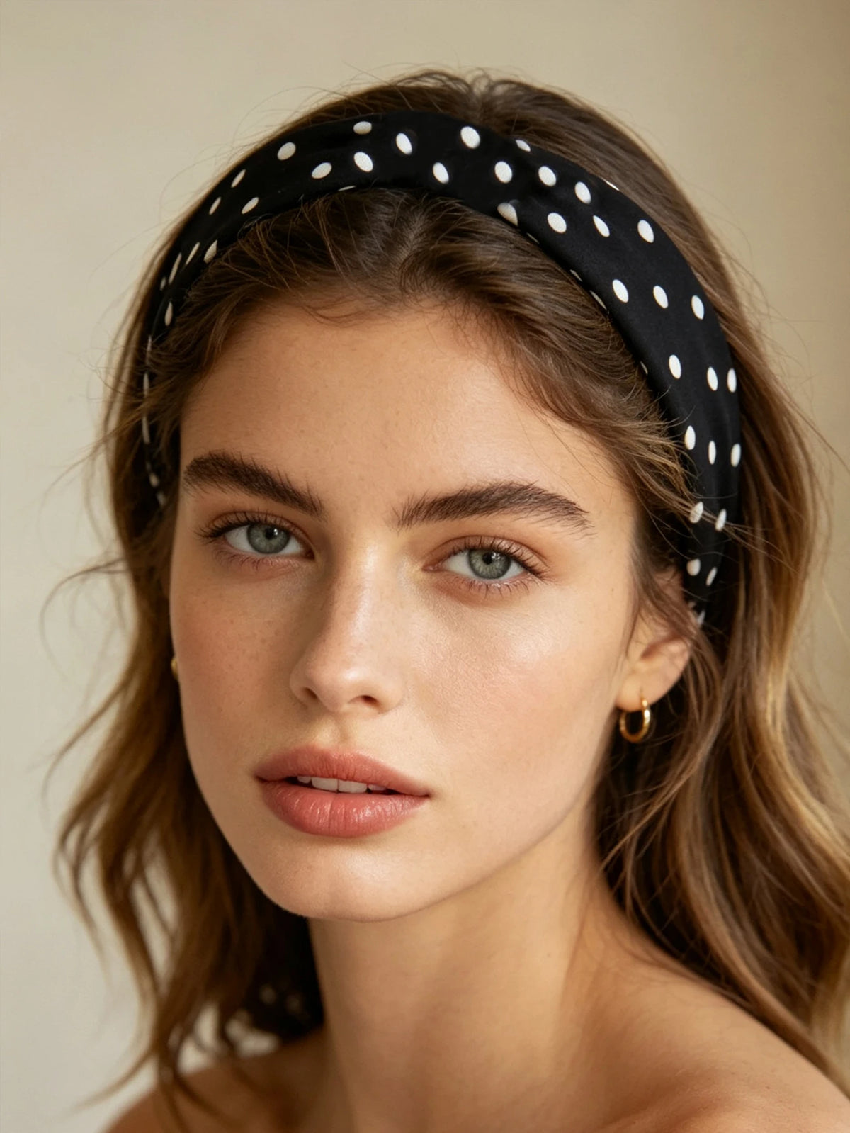 Nahaufnahme einer Frau mit schwarzem Polka-Dot-Haarreif und goldenen Ohrringen.