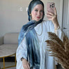 Eine Frau trägt einen blauen Aquarell-Hijab und ein weißes Tunik, posiert drinnen.