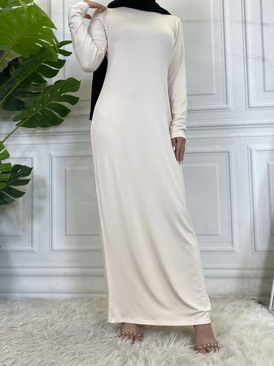 Langes beige Maxi-Abaya-Kleid mit langen Ärmeln und schwarzem Hijab vor weißer Wand