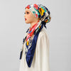 Eine Frau modelliert einen satinbedruckten Turban-Hijab mit floralen Mustern in Rot-, Gelb- und Blautönen.