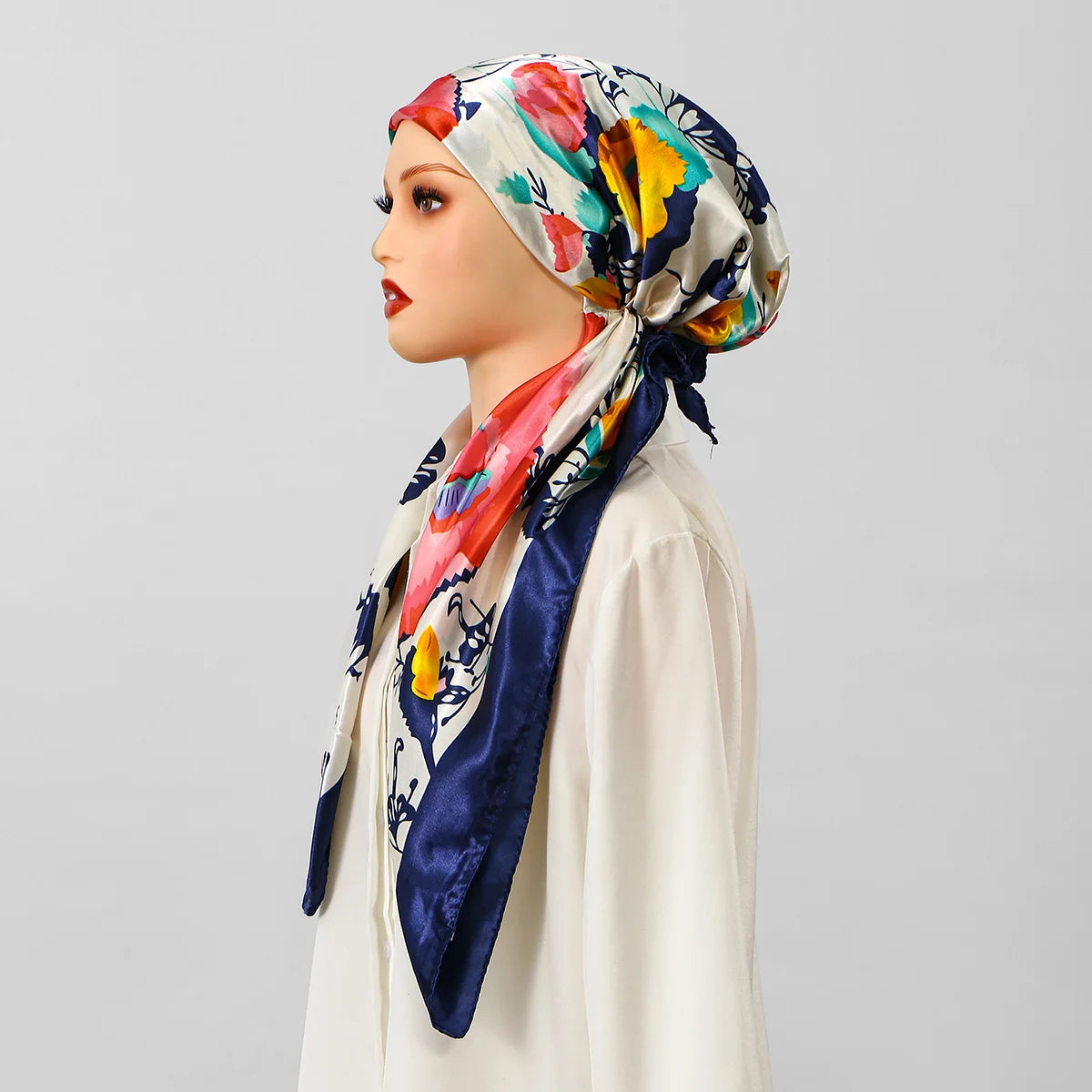 Eine Frau modelliert einen satinbedruckten Turban-Hijab mit floralen Mustern in Rot-, Gelb- und Blautönen.