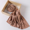 A tan ribbed jersey hijab scarf is draped next to a wooden frame.