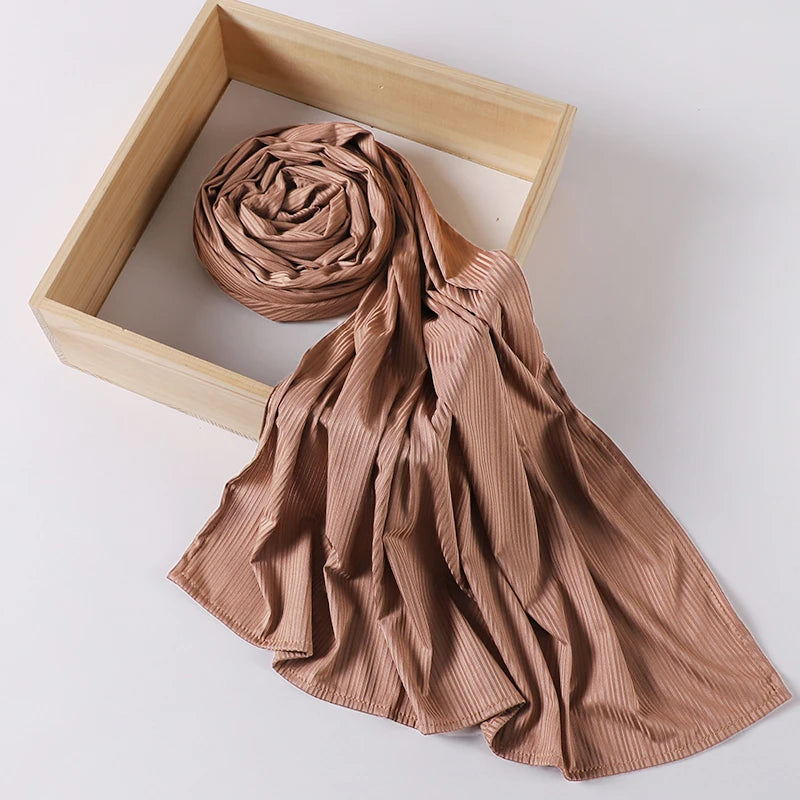 A tan ribbed jersey hijab scarf is draped next to a wooden frame.
