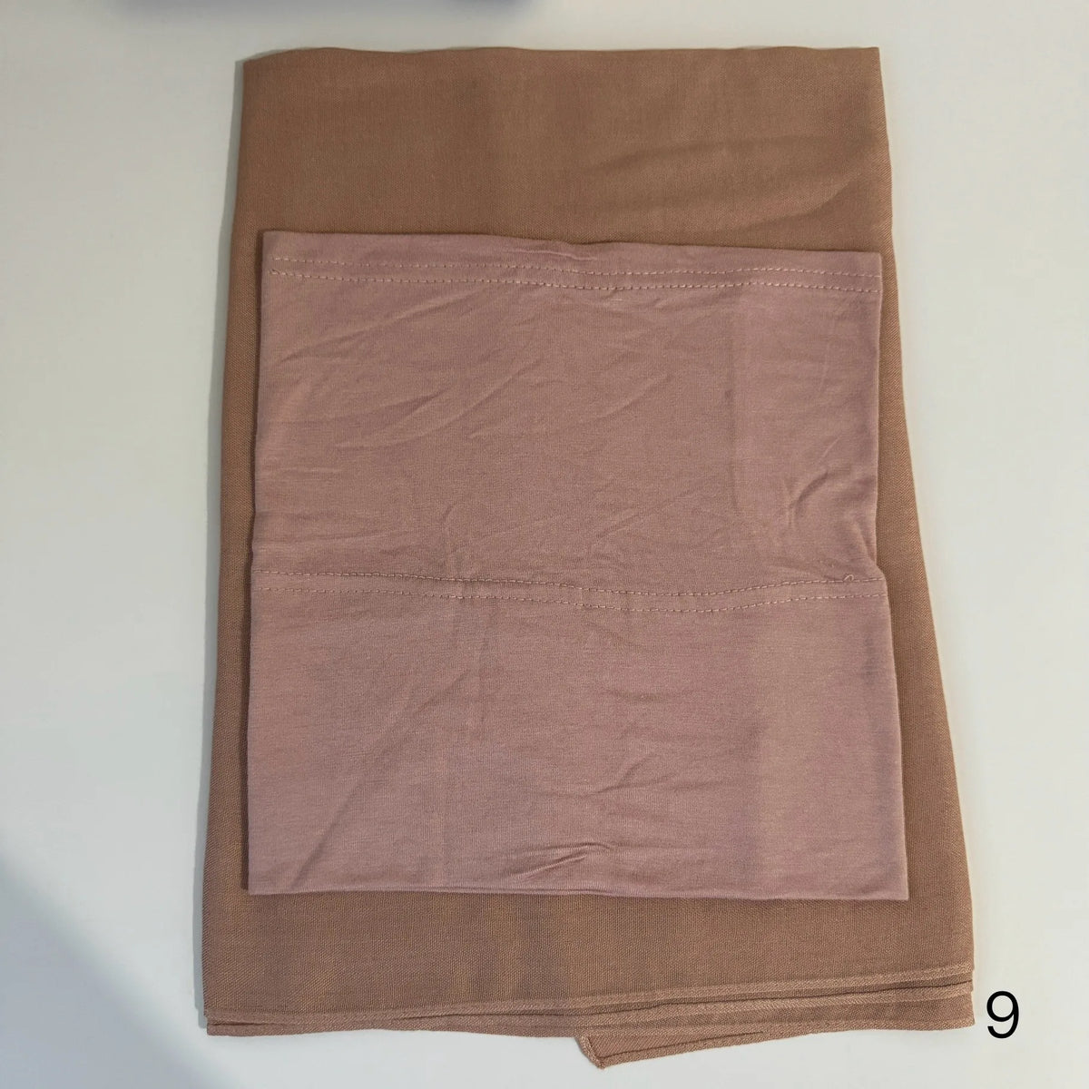 A folded soft mauve hijab set made of a smooth fabric is displayed on a white surface.