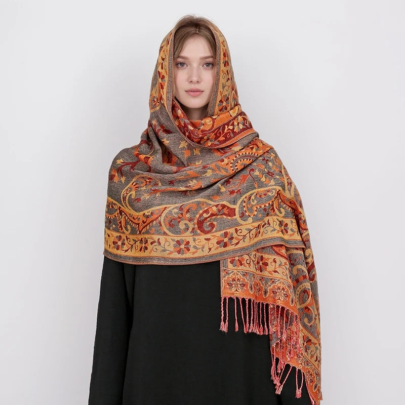 Una mujer vistiendo un pañuelo pashmina lujoso de color naranja y marrón terroso con estampado, drapeado sobre una prenda neg