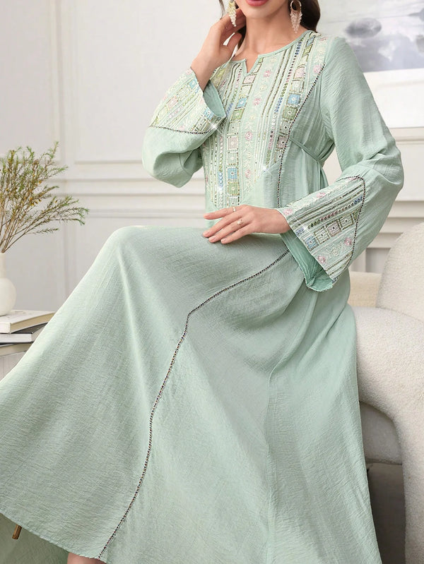 A woman wearing a light green abaya with intricate embroidery and sequins, featuring long sleeves and a flowing silhouette.