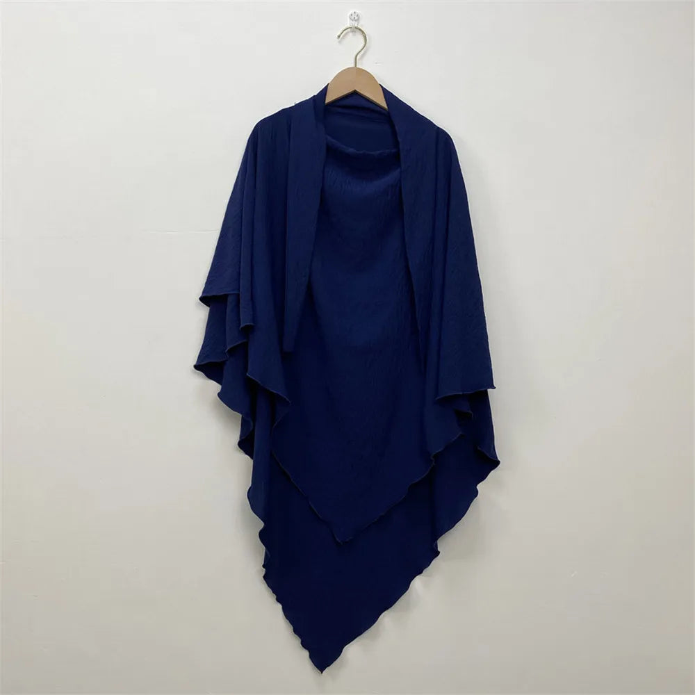A navy blue two-layer everyday hijab scarf draped on a hanger against a white wall.