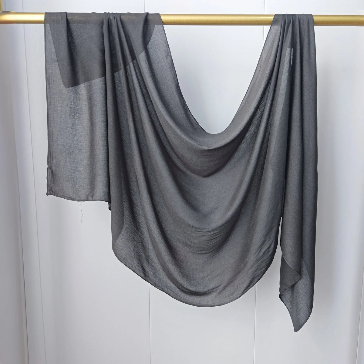 Écharpe de hijab gris uni drapée, suspendue sur une baguette dorée.