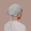 Une femme portant un bonnet de hijab intérieur gris clair à cordon et un haut assorti, vue de profil.