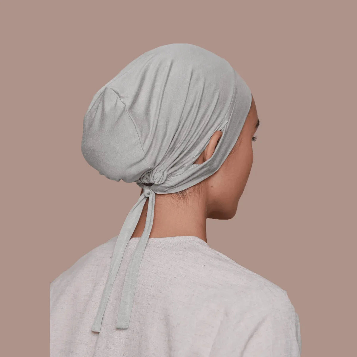 Une femme portant un bonnet de hijab intérieur gris clair à cordon et un haut assorti, vue de profil.