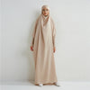 Eine Frau in einem beige, schick verzierten Abaya mit gerafften Ärmeln vor einer weißen Wand.