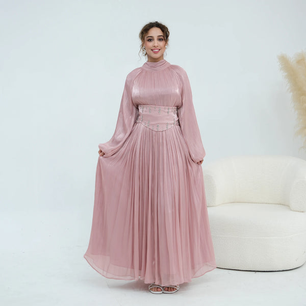 A woman models a flowing dusty rose abaya dress with a high neck and an embellished waist belt.