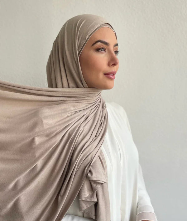 A woman wearing a beige jersey hijab and matching top, looking to the side.