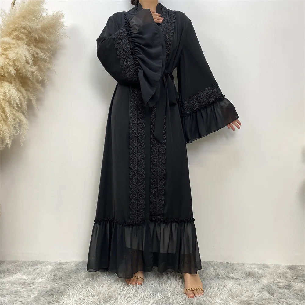 Schwarze, bodenlange Abaya mit Spitzenbesatz und voluminösen Ärmeln vor weißem Hintergrund.