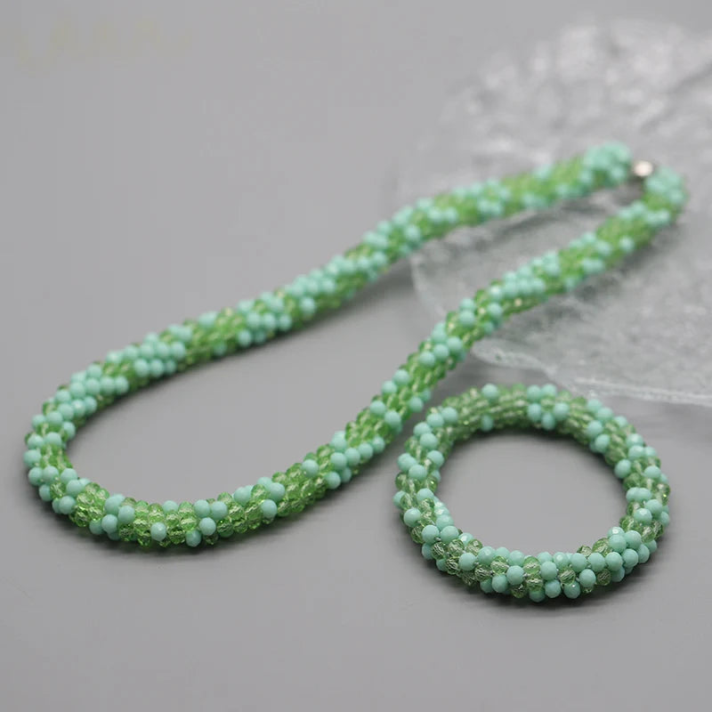 Zarte grüne Perlenkette und Armband auf grauem Hintergrund mit durchscheinendem Stoff.