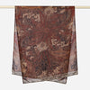 A dark brown printed linen scarf featuring intricate gold floral and paisley patterns hanging on a rod.