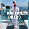 Eine Frau in einem türkisen Kaftan mit goldener Stickerei steht auf einem Boot in der Nähe des Meeres.