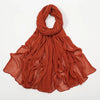 Écharpe à crêpage orange rouille en rayon, drapée autour du cou et flottant sur les épaules.