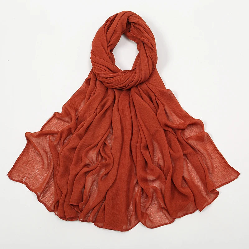 Écharpe à crêpage orange rouille en rayon, drapée autour du cou et flottant sur les épaules.