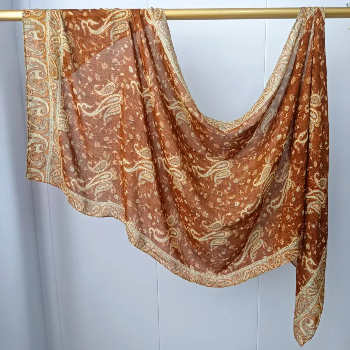 Drapierter, durchscheinender braun-beiger Mehrfarb-Hijab-Schal an einem goldenen Stab hängt.