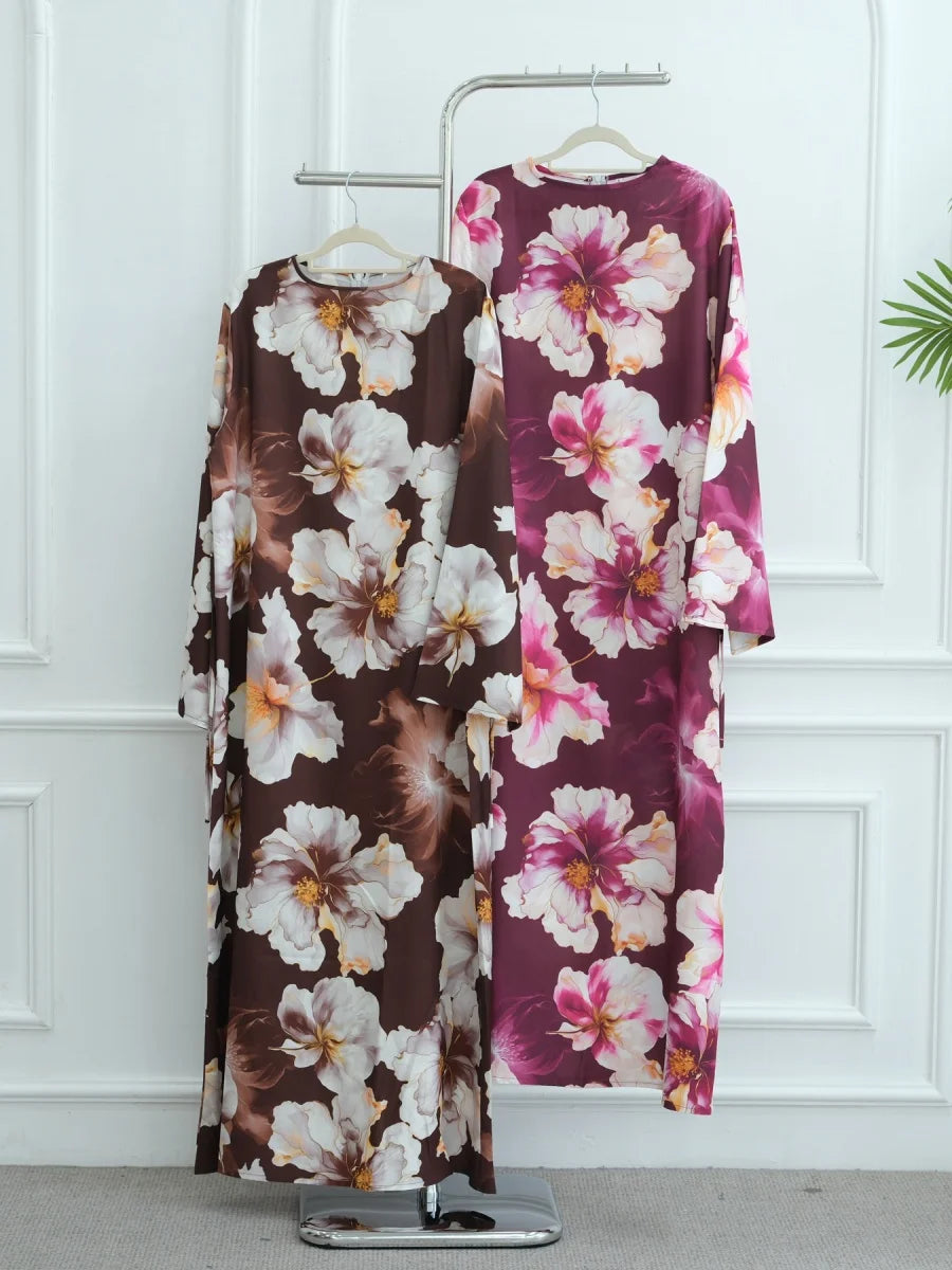 Langes bordeaux-weißes Blumenmuster-Abaya hängt an einem Metallhaken vor einer weißen Wand.