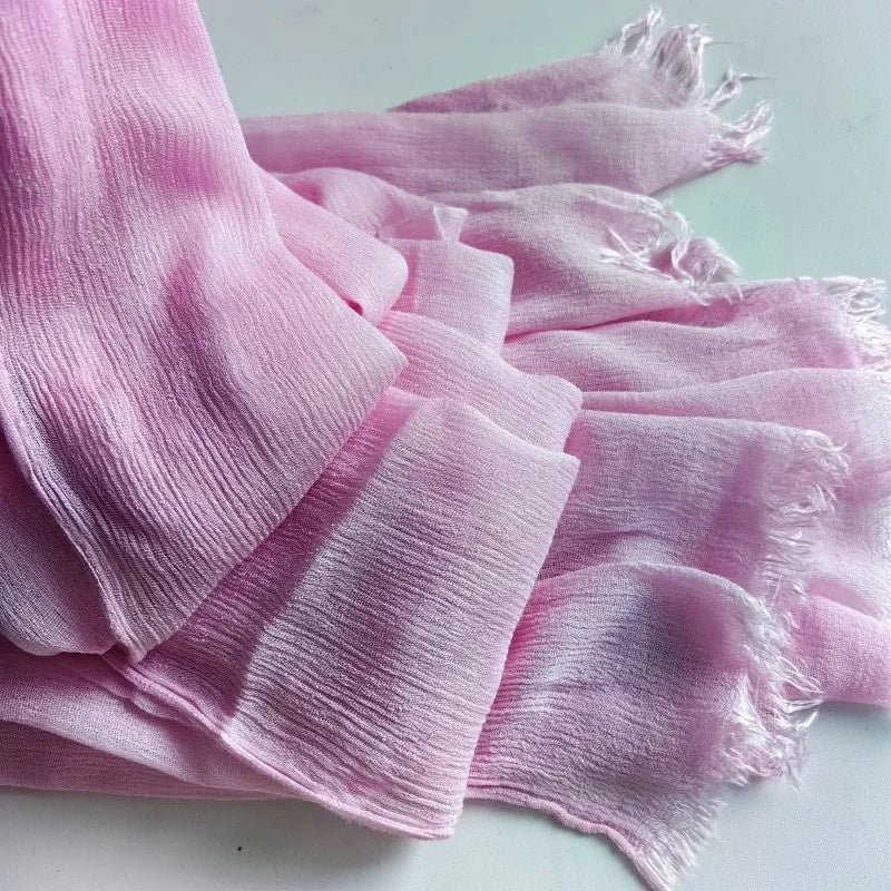 Une pile de foulards de hijab en viscose coton rose pâle avec pompons, posés sur une surface blanche.