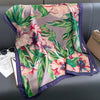 Blaugrünes Blumen-Seidenpareo-Tuch mit Blüten in Pink, Lila und Grün, drapiert auf einem grauen Sofa.