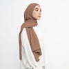 Eine Frau trägt einen beigen weichen Baumwoll-Jersey-Instant-Hijab-Schal und ein weißes Oberteil.