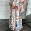 Mujer vistiendo un cárdigan abaya largo y plisado en beige y azul con estampados florales, bufanda color rosa empolvado y mar