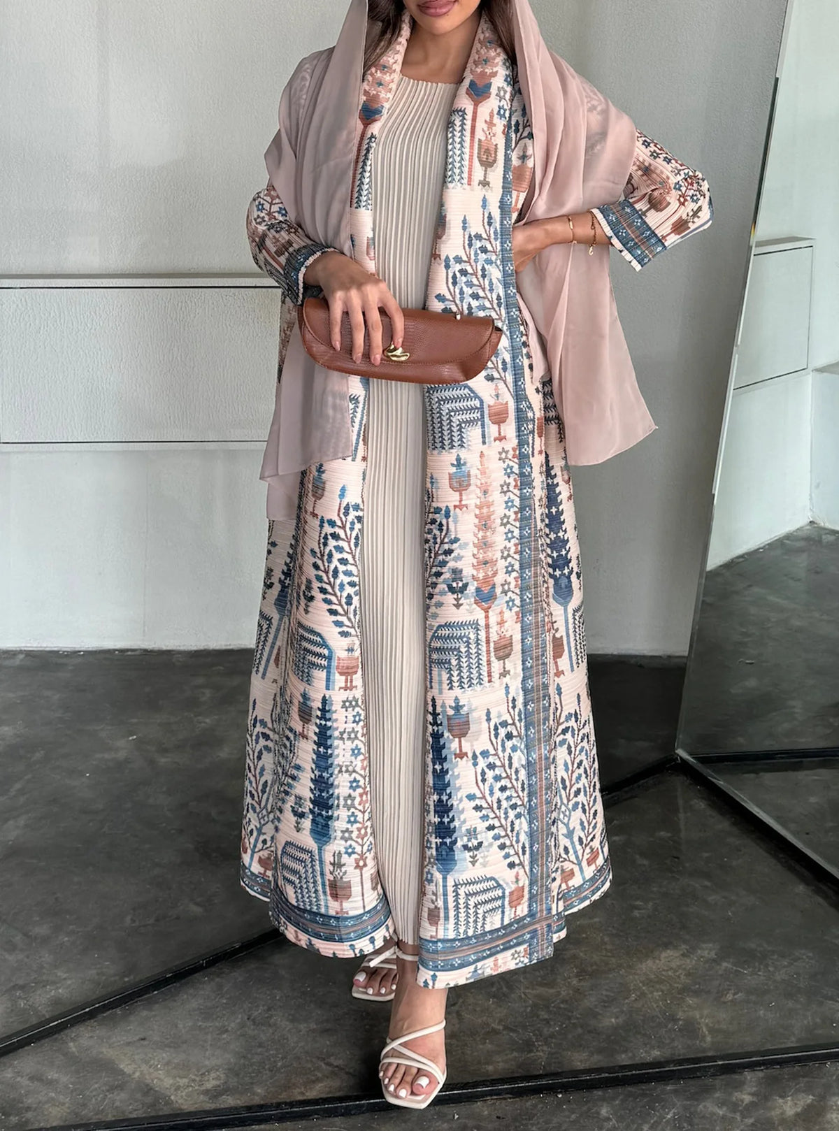 Mujer vistiendo un cárdigan abaya largo y plisado en beige y azul con estampados florales, bufanda color rosa empolvado y mar