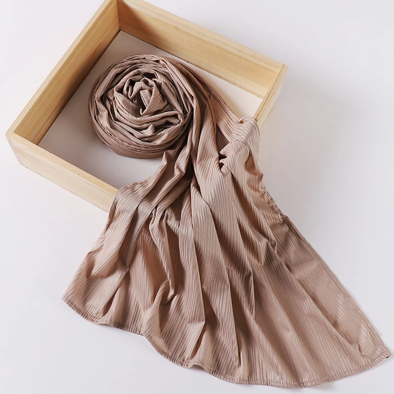 A beige ribbed jersey hijab scarf is rolled and draped within a light wooden frame.