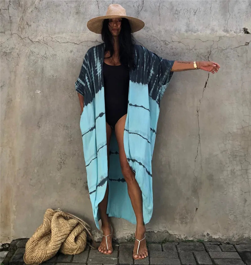 Eine Frau in einem hellblauen gemusterten Kimono-Überwurf über einem schwarzen Kleid und einem Strohhut vor einer strukturier