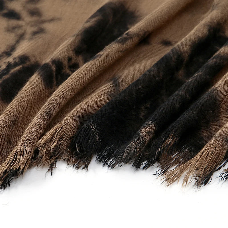Primer plano de una bufanda de tela tie-dye marrón ombre con tonos negros y beige, con bordes de flecos.