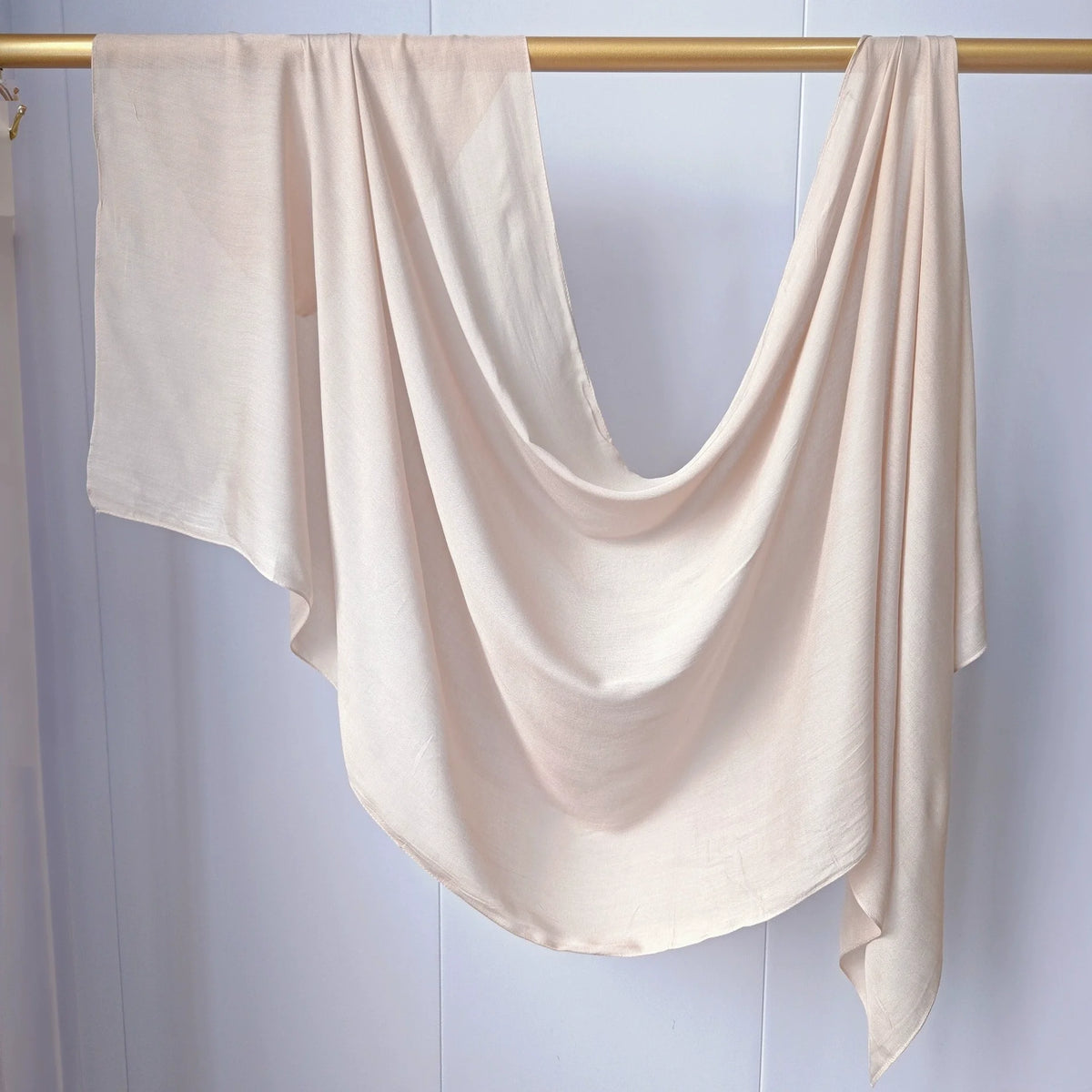 Foulard modal de couleur beige clair drapé sur un cintre en bois.