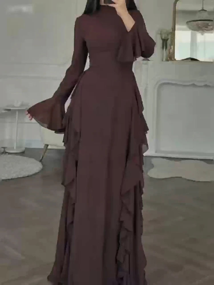 A full-length, dark plum maxi dress with a high neckline and long sleeves, featuring ruffled details.
