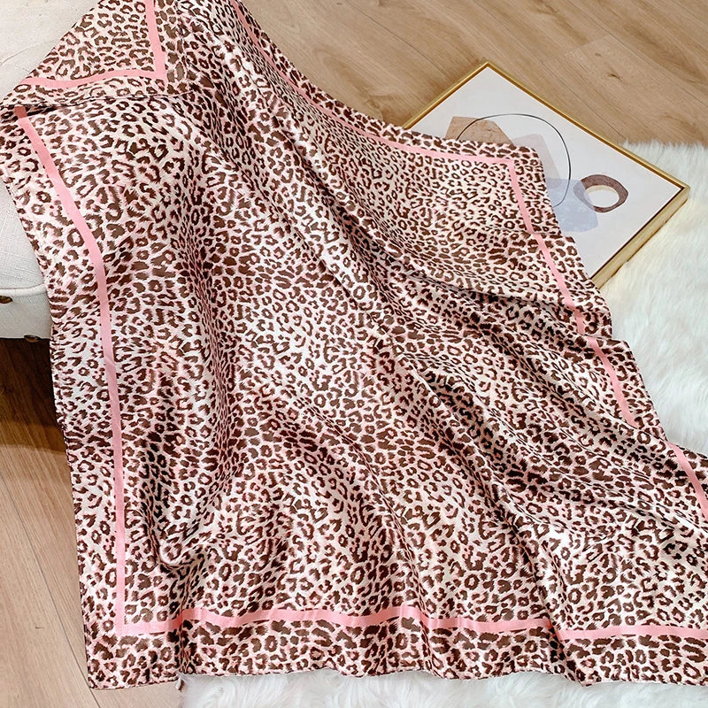 A flowing leopard print silk satin scarf draped on a white surface next to a framed picture.