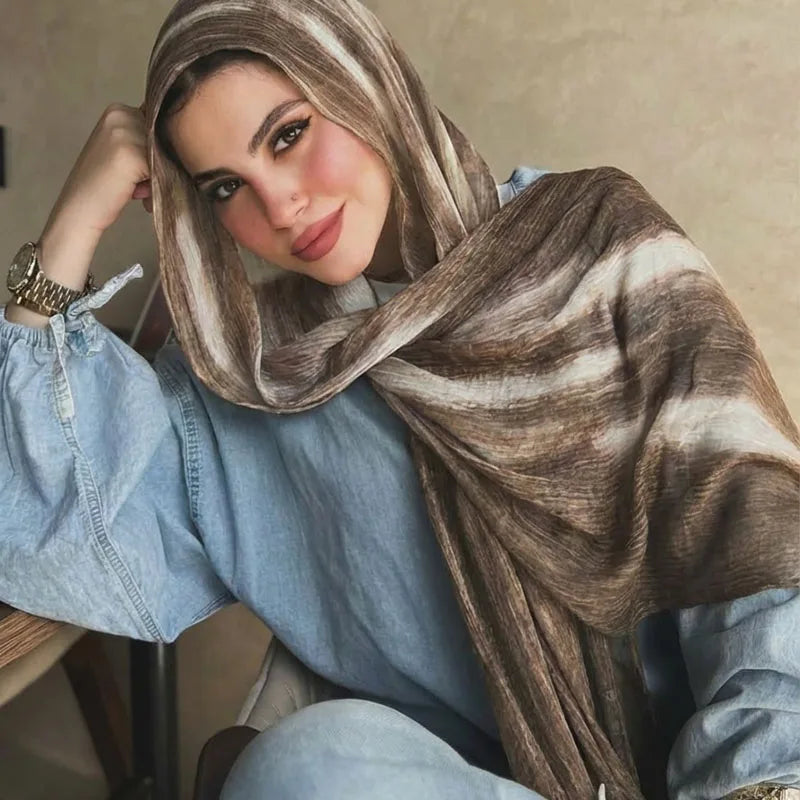 Una mujer vistiendo un pañuelo hijab de estampado acuarela marrón y beige sobre una camisa vaquera azul claro.