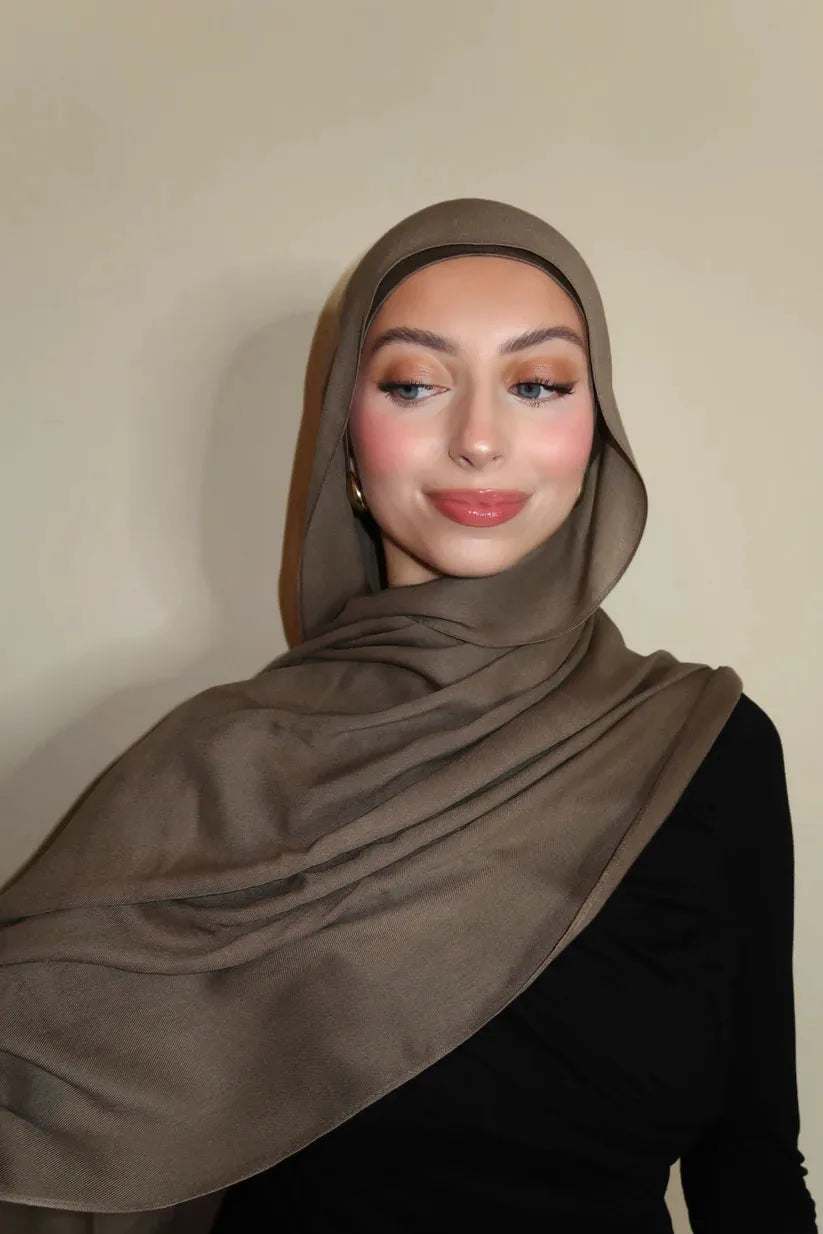 Eine Frau trägt einen einfarbigen braunen Gradient-Rayon-Hijab und schwarze Kleidung.