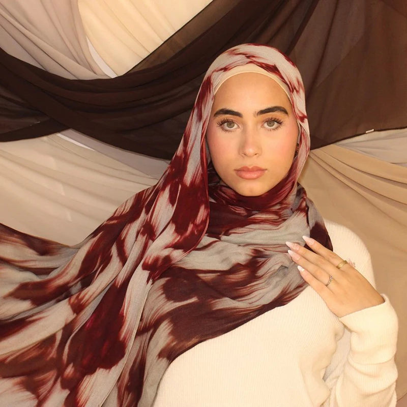 Eine Frau trägt einen braun-weißen Aquarellblumenmuster-Hijabschal über ihren Kopf und ihre Schultern.