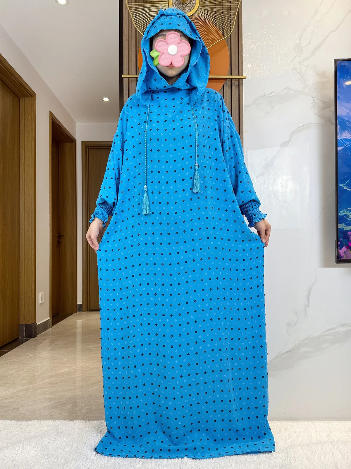 Una mujer vistiendo una abaya de algodón azul brillante con puntos negros y una mascarilla de flor rosa.