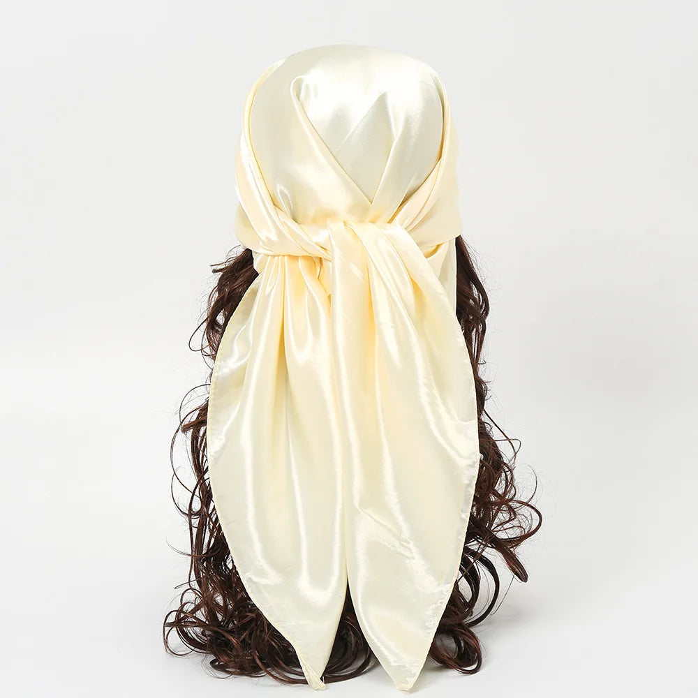 A cream-colored silk satin hijab scarf tied in a knot, draped over dark curly hair.