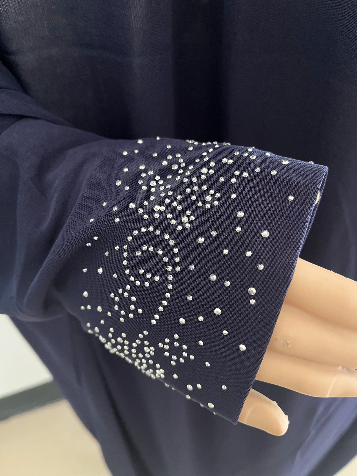 Gros plan sur une manche de caftan bleu marine avec broderie à pois blancs.