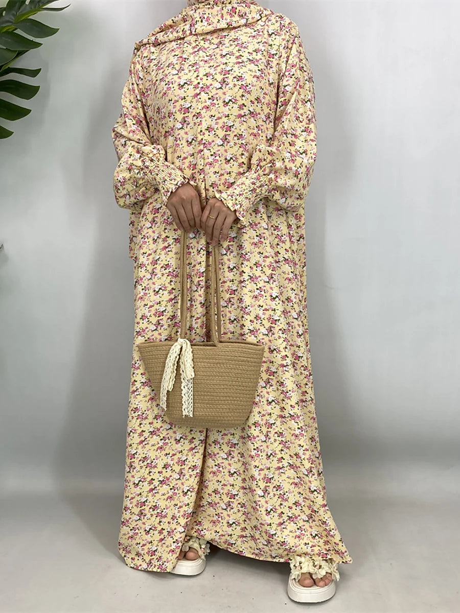 Una mujer vistiendo una elegante caftán abaya floral en tonos amarillo pálido y rosa, combinada con un bolso de paja tejido.