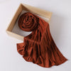 A rust-colored ribbed jersey hijab scarf is draped within a light wooden frame.
