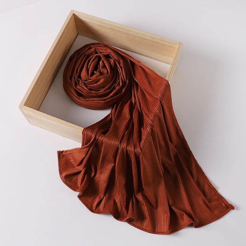 A rust-colored ribbed jersey hijab scarf is draped within a light wooden frame.