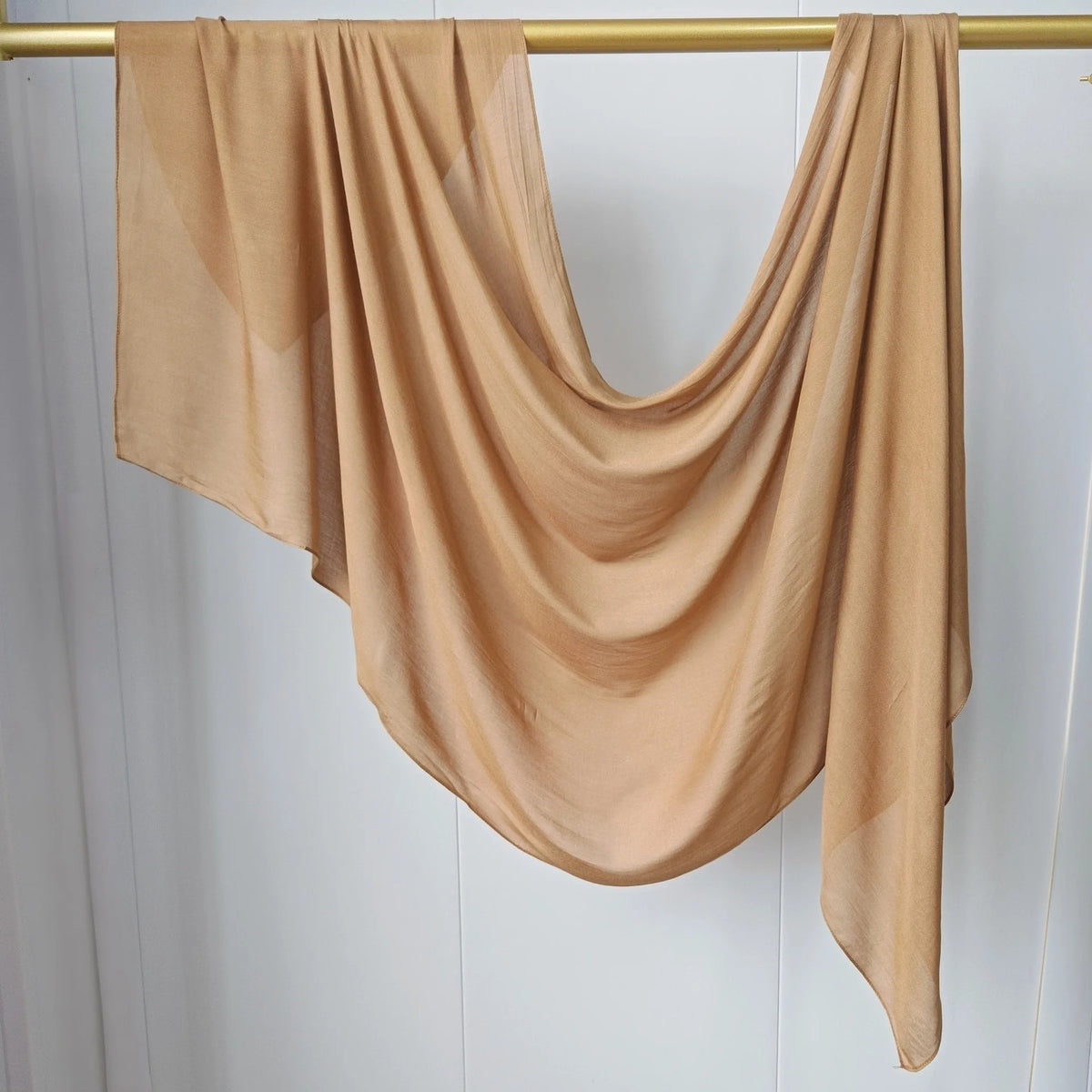 Foulard hijab uni beige drapé sur un cintre doré.