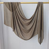 Un foulard modal marron uni drapé, suspendu sur une perche dorée contre un mur blanc.
