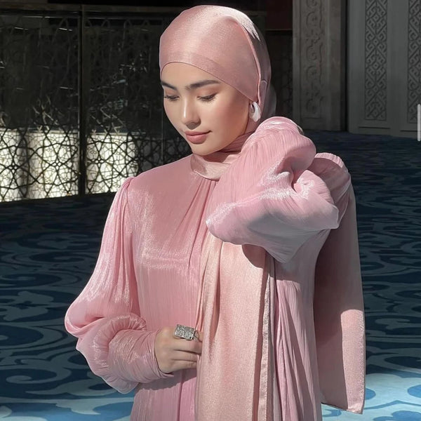 A woman wearing a light pink, crinkled chiffon shawl hijab with long sleeves and a matching top.