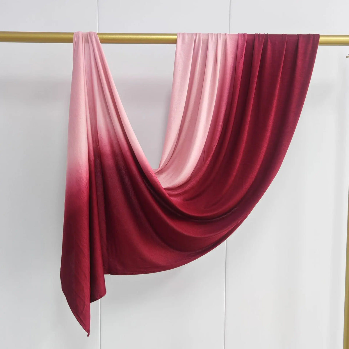 Pañuelo de chifón de algodón doble cara en degradado rosa y rojo intenso colgado en un soporte.