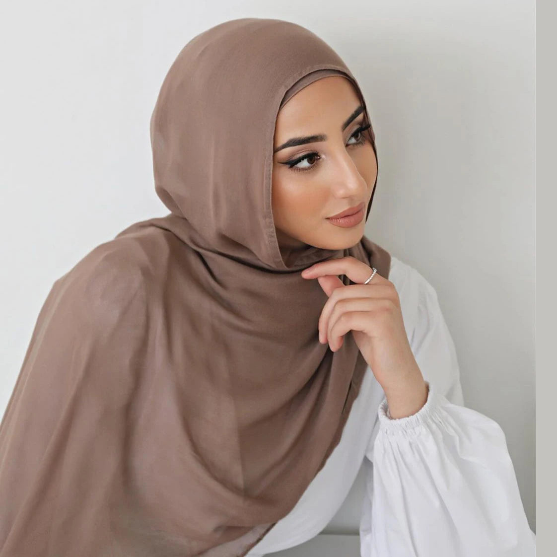 Una mujer vistiendo un chal hiyab de algodón rayón marrón liso con una blusa blanca.